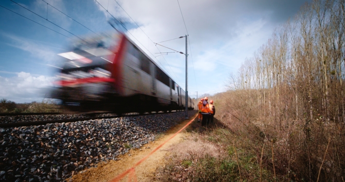 Photo d'un train roulant avec des techniciens de l'ONF en bord de voie