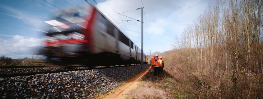 Photo d'un train roulant avec des techniciens de l'ONF en bord de voie