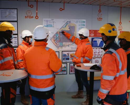 Photo de compagnons dans un algeco de chantier en train de faire une réunion avec le plan du bâtiment