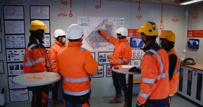 Photo de compagnons dans un algeco de chantier en train de faire une réunion avec le plan du bâtiment