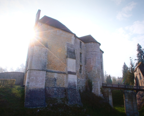 Vue du château d'Harcourt et de son pont en bois, avec le soleil levant et pointant derrière lui.