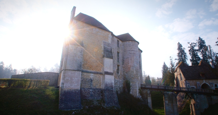 Vue du château d'Harcourt et de son pont en bois, avec le soleil levant et pointant derrière lui.