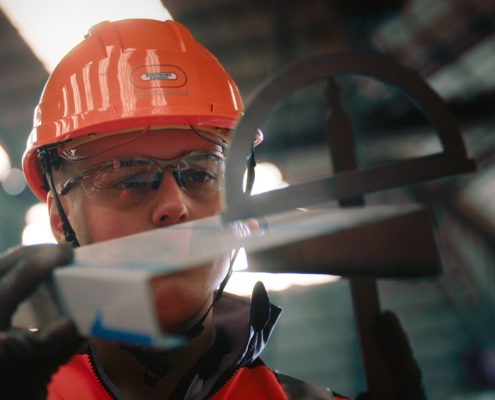 Photo d'un chef de chantier avec casque et gants, regardant en détail un élément de construction en métal.