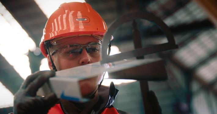 Photo d'un chef de chantier avec casque et gants, regardant en détail un élément de construction en métal.