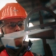 Photo d'un chef de chantier avec casque et gants, regardant en détail un élément de construction en métal.