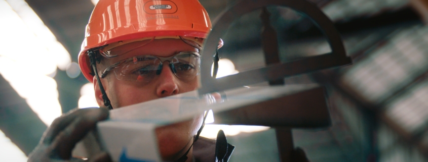 Photo d'un chef de chantier avec casque et gants, regardant en détail un élément de construction en métal.